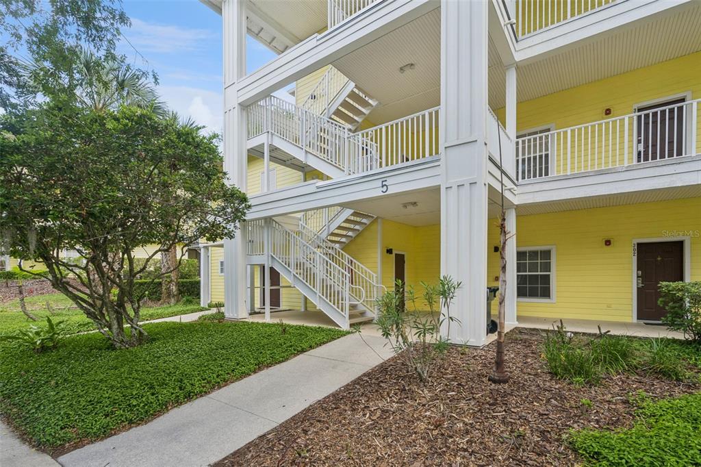 A yellow multi-story apartment building features an exterior staircase and a concrete walkway — 313 LUCAYA LOOP, DAVENPORT, FL