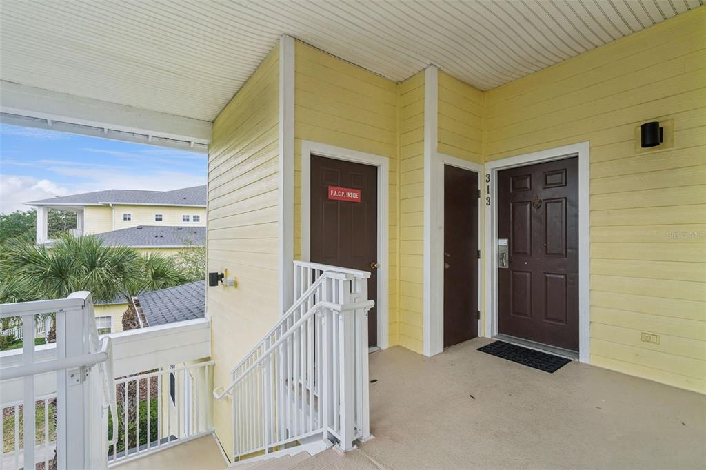 An exterior view of a yellow building landing with two brown doors and stairs — 313 LUCAYA LOOP, DAVENPORT, FL