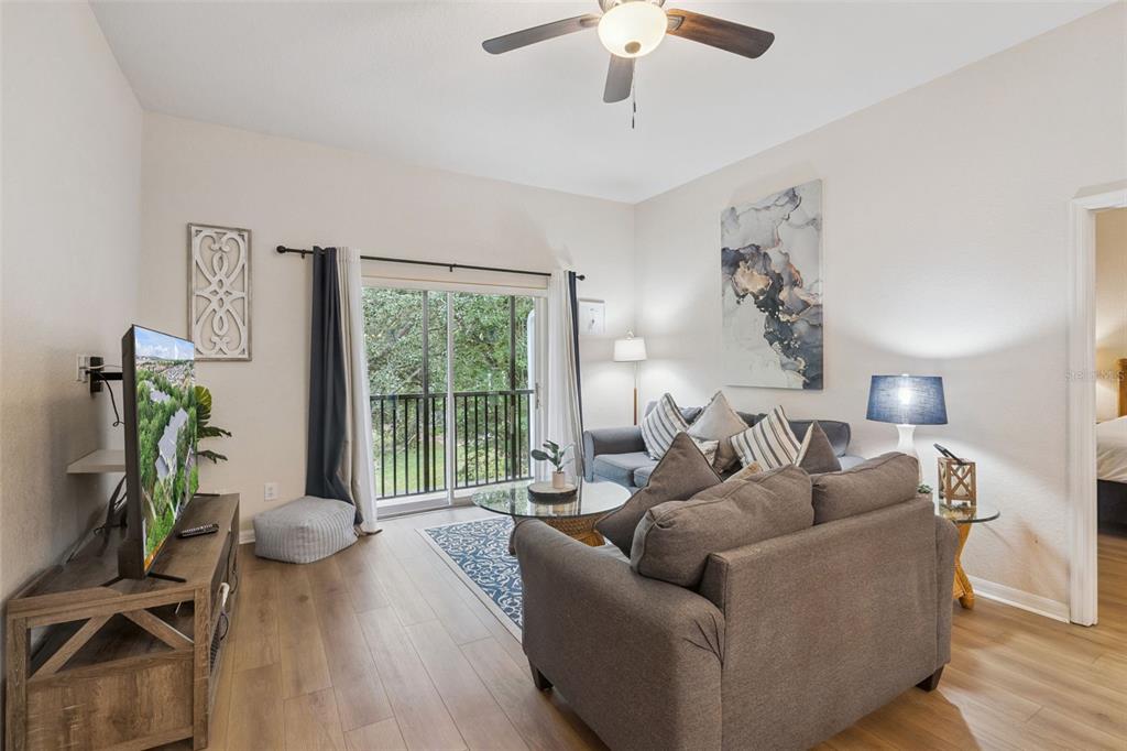 A living room features wood-look flooring, a gray sofa, a ceiling fan, and a balcony — 313 LUCAYA LOOP, DAVENPORT, FL