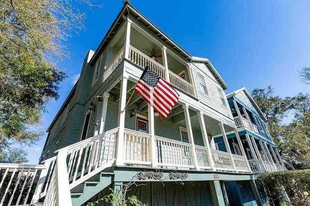 A low-angle exterior view of a multi-story house with double-decker porches and an American flag — 204 VIRGINIA AVENUE, STEINHATCHEE, FL
