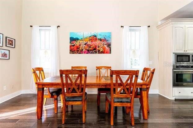 A dining room features a wooden table with six chairs, white curtains, and wall art — 204 VIRGINIA AVENUE, STEINHATCHEE, FL