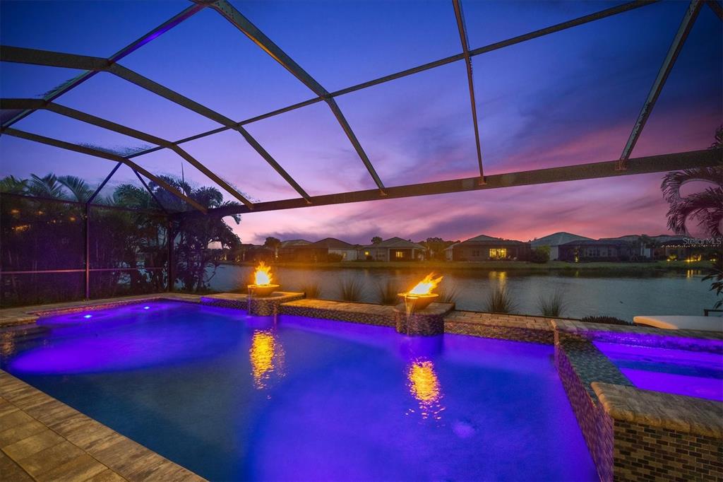 A swimming pool with fire bowls and purple lighting sits inside a screened-in lanai — 3214 ANCHOR BAY TRAIL, BRADENTON, FL