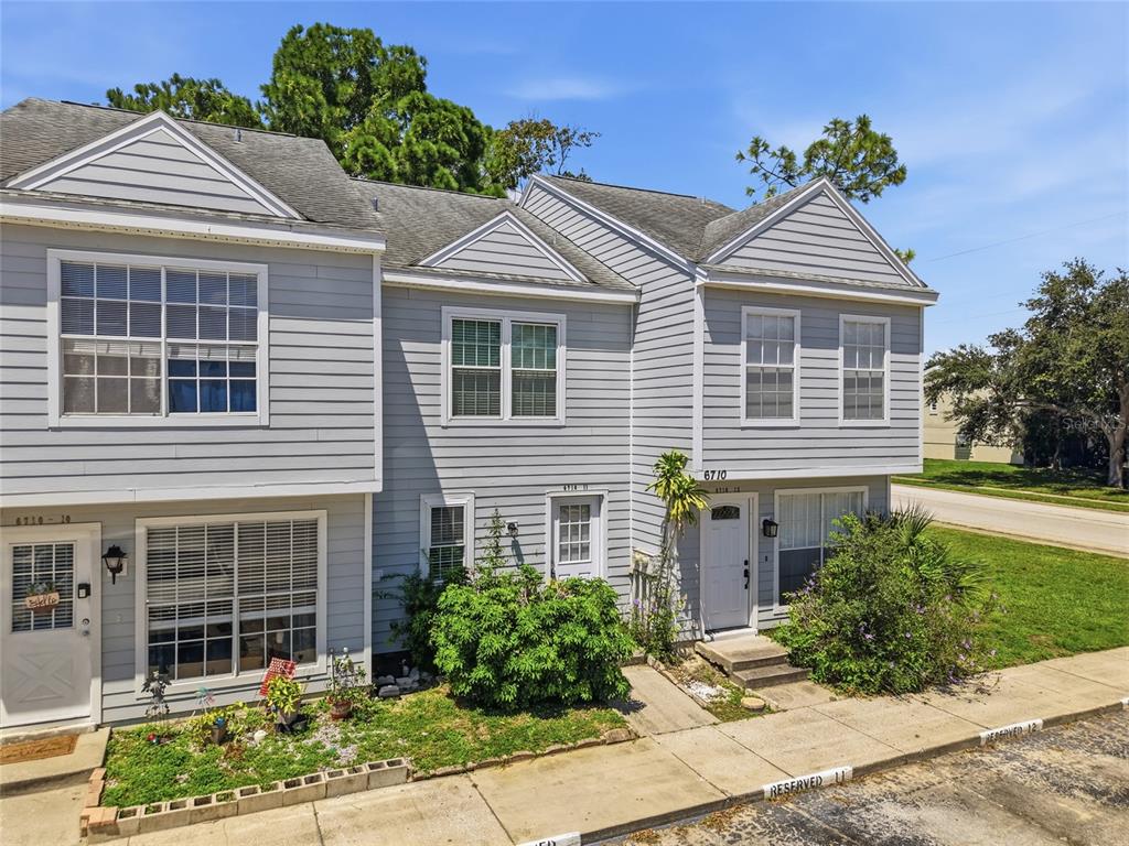 A two-story gray townhouse exterior features multiple windows, white doors, and a small front garden — 6710 121ST AVENUE UNIT 11, LARGO, FL