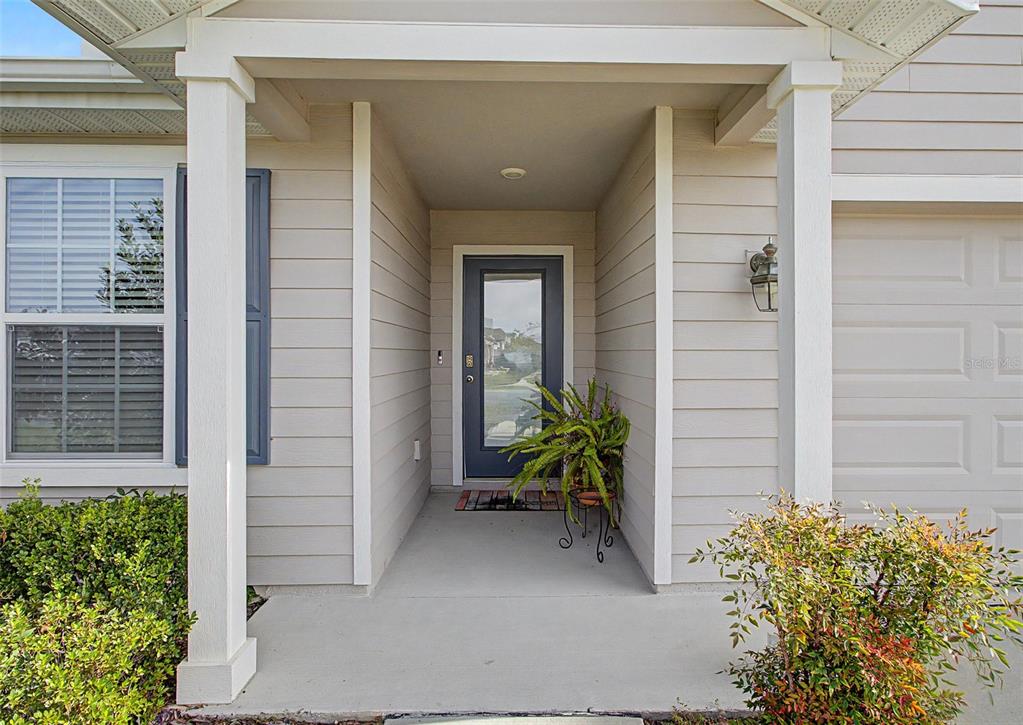 A covered entryway features a gray front door with a glass panel and a potted plant — 25199 NW 8TH ROAD, NEWBERRY, FL