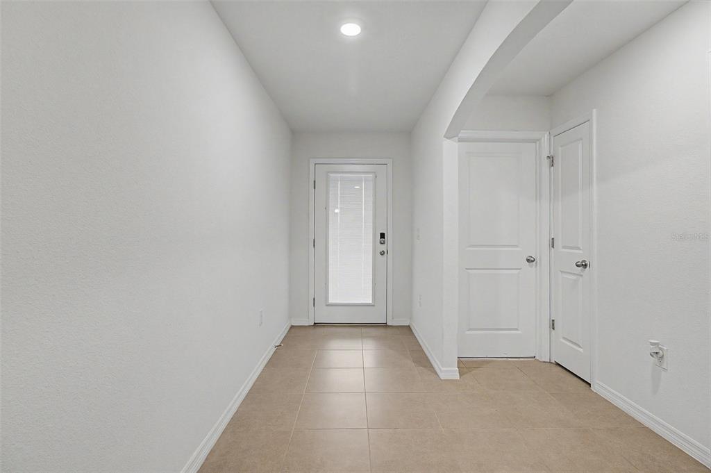 A hallway with white walls, tile flooring, a glass-paneled door, and two interior doors — 25199 NW 8TH ROAD, NEWBERRY, FL