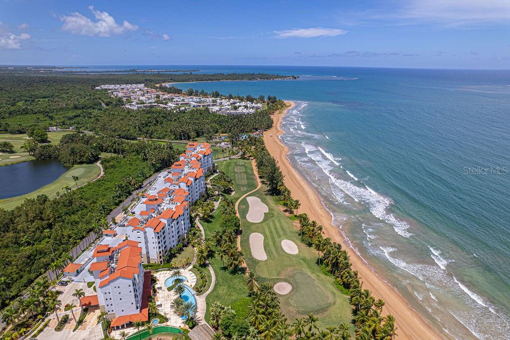 An aerial view shows a multi-story apartment complex situated next to a golf course and beach — Ocean Sixteen 9000 RIO MAR BLVD UNIT 321, RIO GRANDE, PR