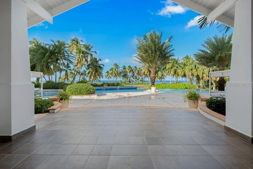A covered patio overlooks a swimming pool, palm trees, and the ocean — Ocean Sixteen 9000 RIO MAR BLVD UNIT 321, RIO GRANDE, PR