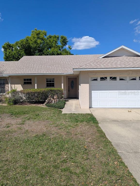A single-story house features a beige stucco exterior, a white garage door, and a front walkway — 108 TWIN LAKE CIRCLE, UMATILLA, FL