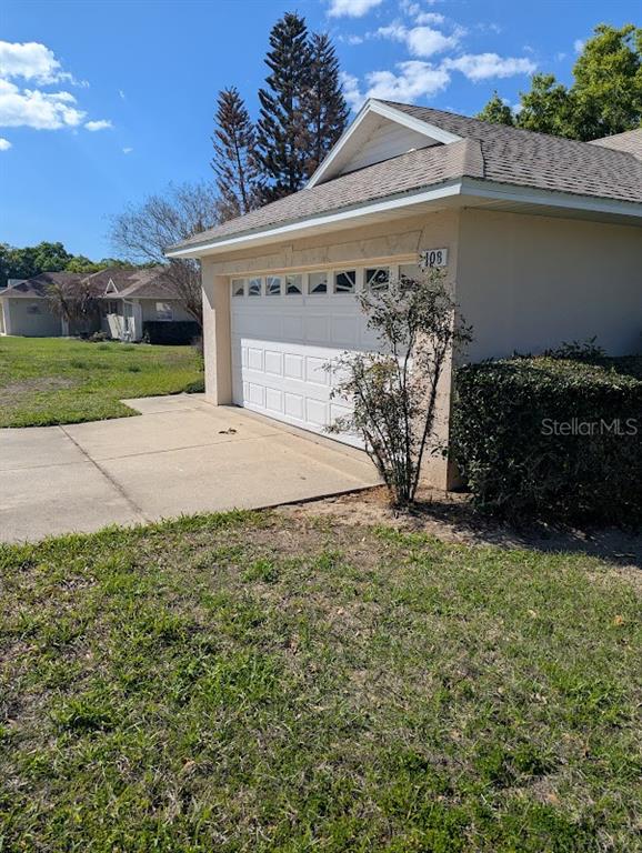 A tan house with a white garage door and a concrete driveway under a blue sky — 108 TWIN LAKE CIRCLE, UMATILLA, FL