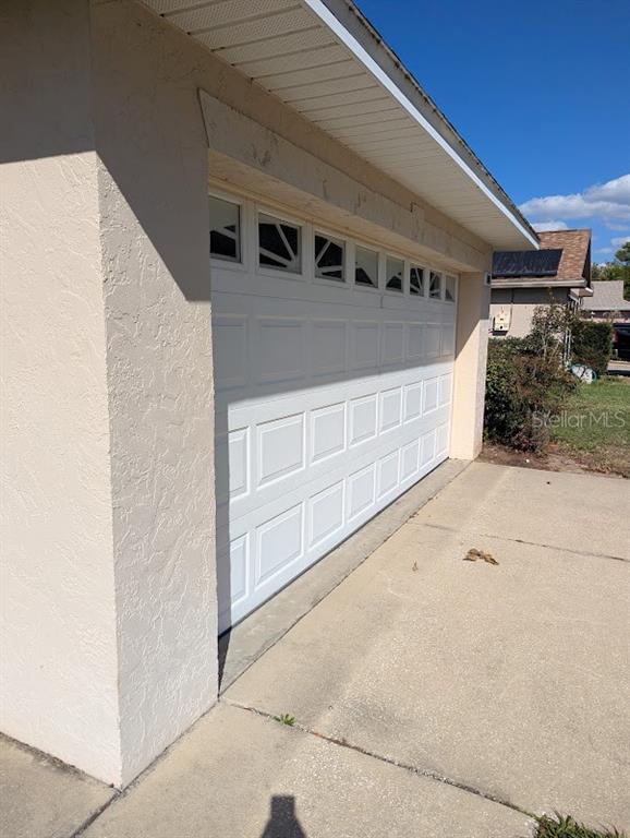 A white garage door with decorative windows is set into a beige stucco exterior wall — 108 TWIN LAKE CIRCLE, UMATILLA, FL
