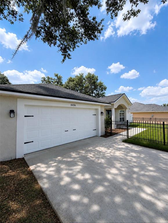 A view of a house exterior featuring a white garage door and a metal fence — 10058 SE 105TH PLACE, BELLEVIEW, FL