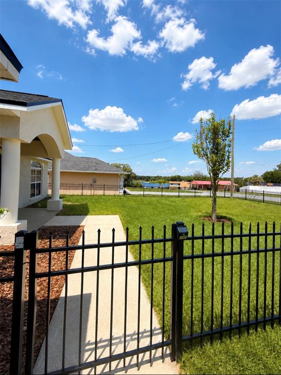 A black metal fence encloses a grassy backyard with a sidewalk and a single tree — 10058 SE 105TH PLACE, BELLEVIEW, FL