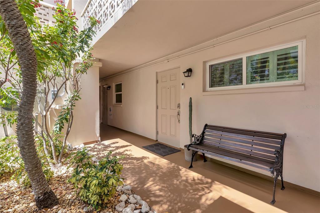 A covered outdoor entryway features a white door, a black bench, and a small tree — 620 EDGEWATER DRIVE UNIT 102, DUNEDIN, FL
