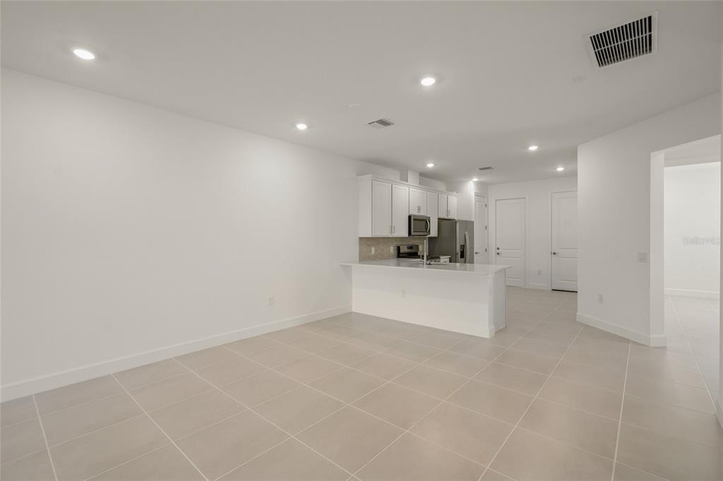 A bright, open-concept kitchen features white cabinets, stainless steel appliances, and light-colored tile flooring — 14860 MISTY POND LOOP, NOKOMIS, FL