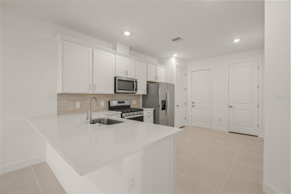 A modern kitchen features white cabinets, quartz countertops, stainless steel appliances, and light tile flooring — 14860 MISTY POND LOOP, NOKOMIS, FL