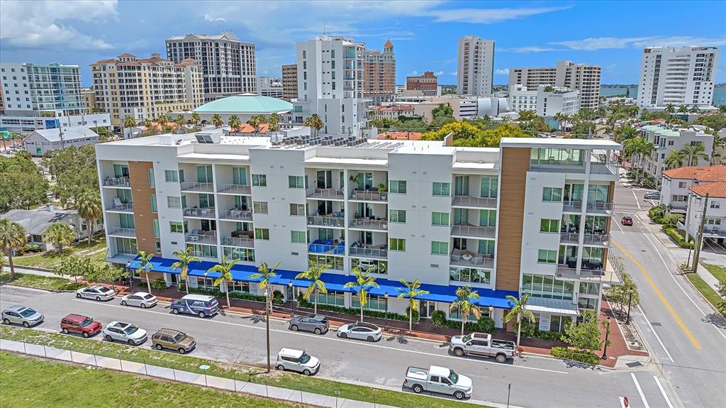 An aerial view of a modern multi-story apartment building with balconies and a blue awning — 332 COCOANUT AVENUE UNIT 406, SARASOTA, FL
