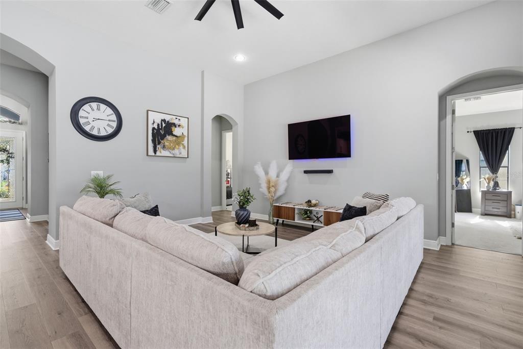 A living room features a large sectional sofa, a wall-mounted television, and wood-look flooring — 13819 MOONSTONE CANYON DRIVE, RIVERVIEW, FL