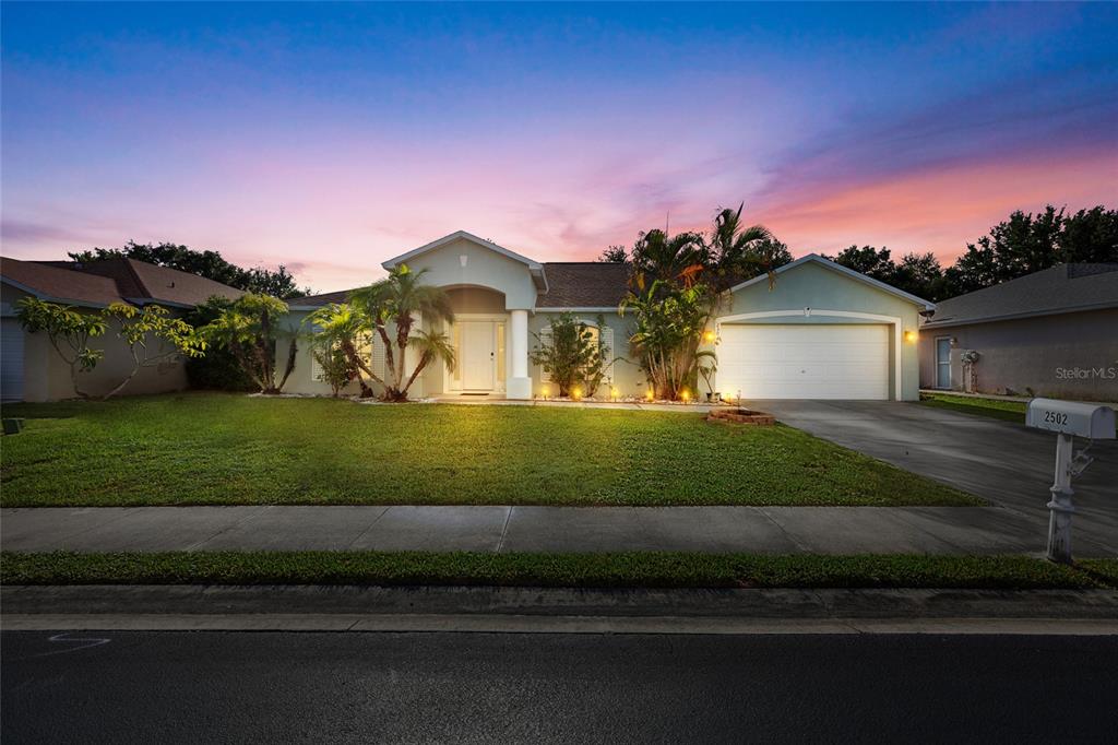 A single-story house with a white garage, palm trees, and a green lawn at sunset — 2502 NATURE POINTE LOOP, FORT MYERS, FL