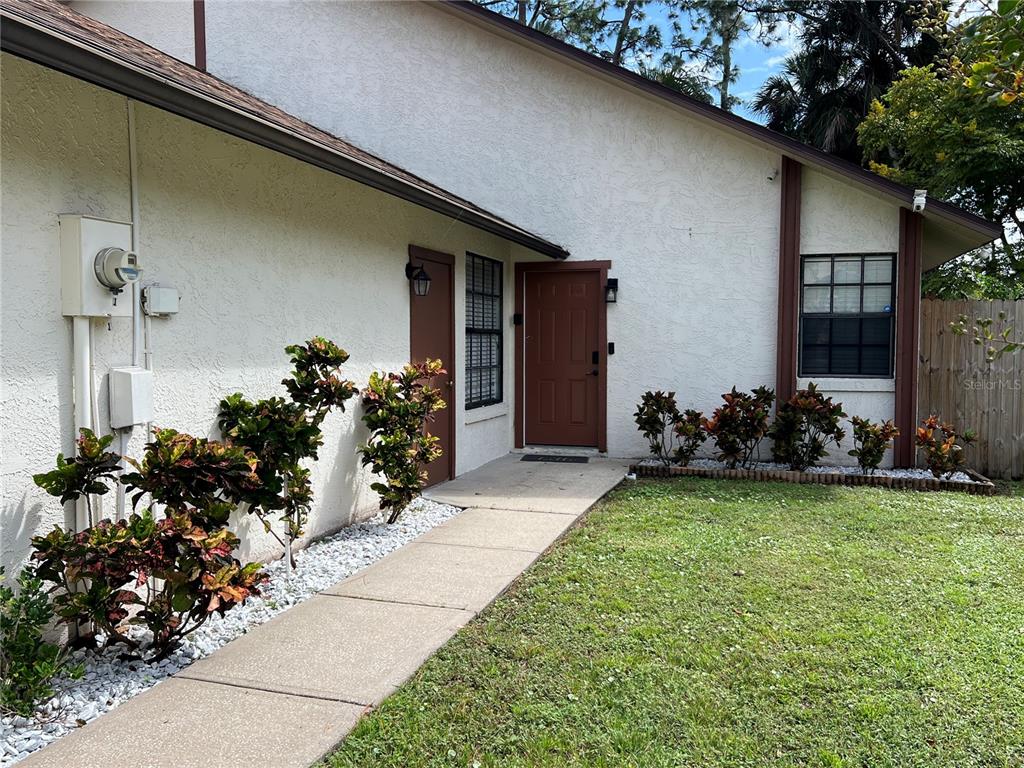 The exterior of a house features a concrete walkway, brown doors, and landscaped shrubs — 962 STONYBROOK CIRCLE, PORT ORANGE, FL