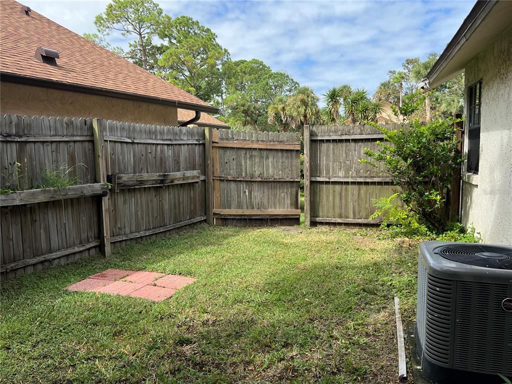 A backyard features a wooden privacy fence, a small patch of grass, and an HVAC unit — 962 STONYBROOK CIRCLE, PORT ORANGE, FL