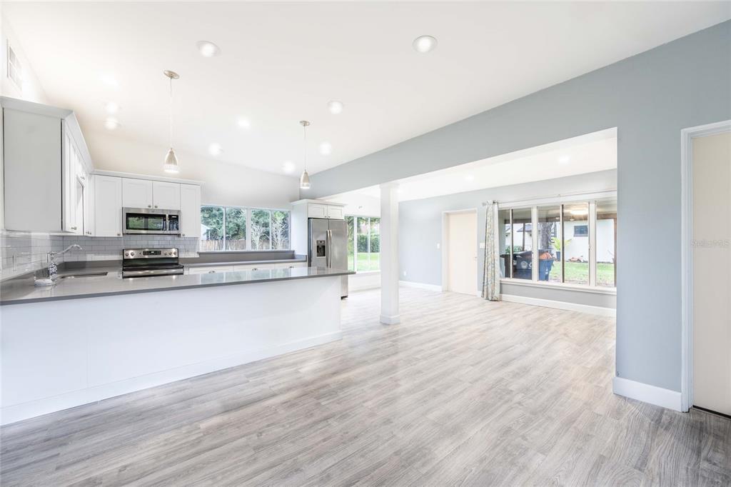 A bright, open-concept kitchen and living area featuring white cabinetry, gray countertops, and wood-look flooring — 2231 NAIRN DRIVE, WINTER PARK, FL