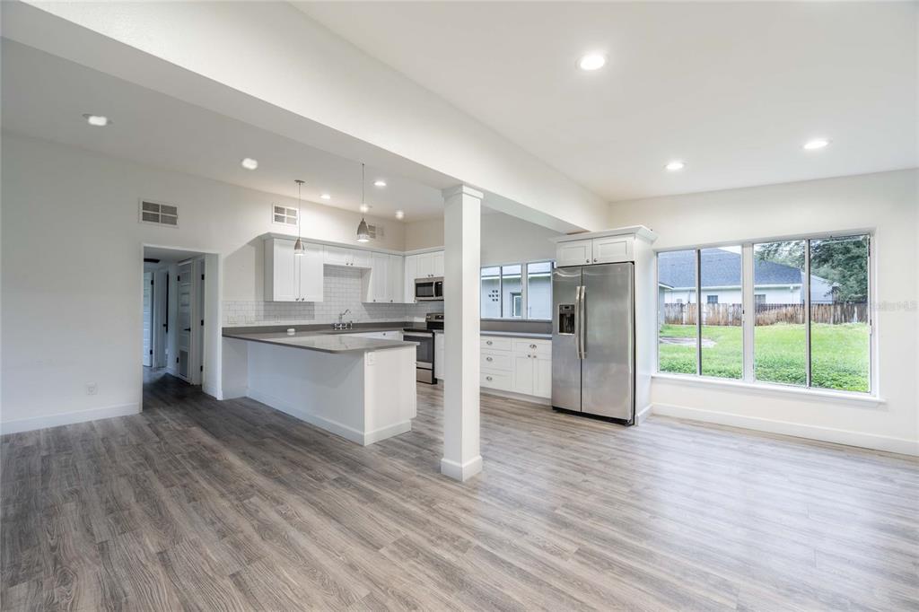A kitchen with white cabinets, stainless steel appliances, and gray flooring opens to a living area — 2231 NAIRN DRIVE, WINTER PARK, FL