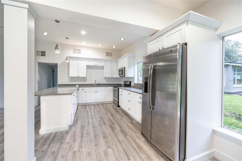 A modern kitchen with white cabinets, stainless steel appliances, and gray wood-look flooring — 2231 NAIRN DRIVE, WINTER PARK, FL