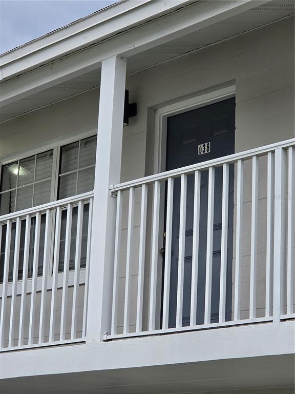 A white balcony with a railing sits outside a dark door labeled 038 — 1400 EUDORA ROAD UNIT D-38, MOUNT DORA, FL