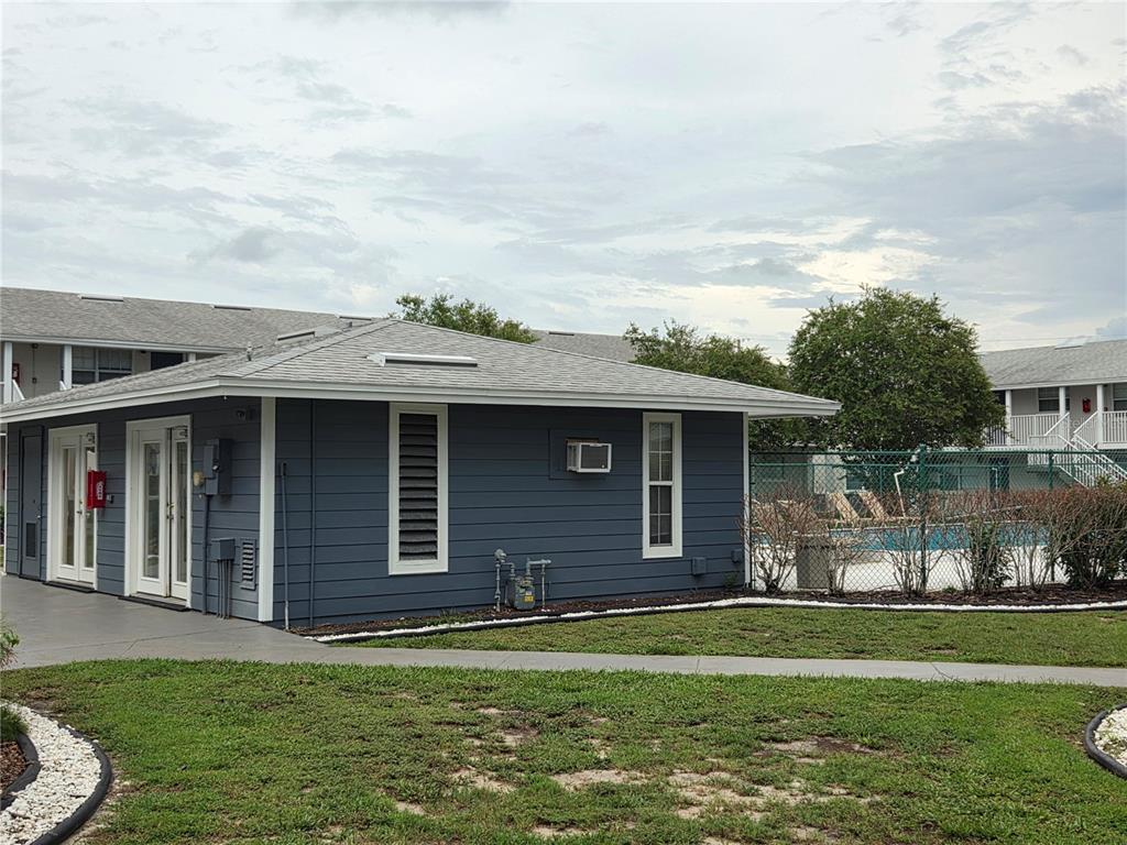 A gray, single-story building with a shingled roof stands next to a fenced swimming pool — 1400 EUDORA ROAD UNIT D-38, MOUNT DORA, FL
