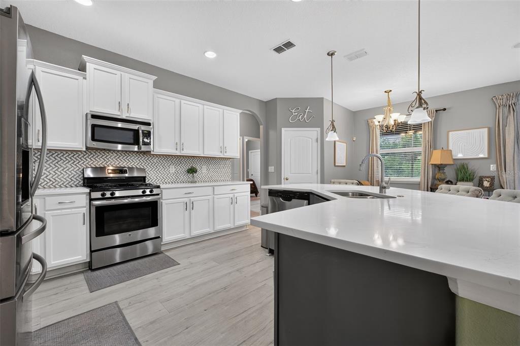 A kitchen features white cabinets, stainless steel appliances, and a herringbone-patterned tile backsplash — 1458 DAYSTAR LANE, DELTONA, FL