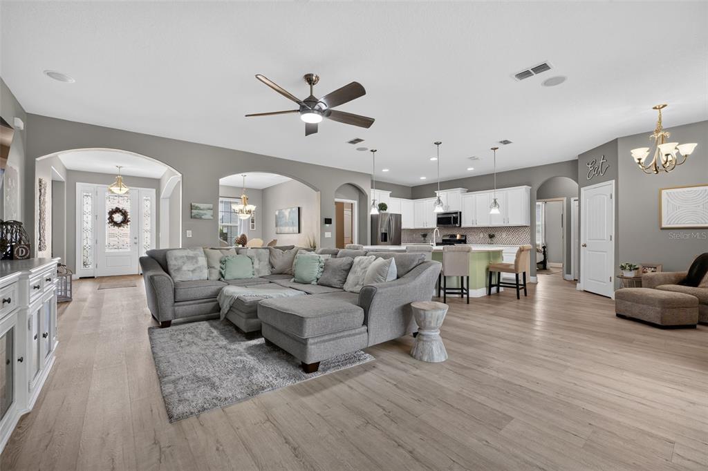 An open-concept living room and kitchen featuring gray walls, light wood flooring, and white cabinetry — 1458 DAYSTAR LANE, DELTONA, FL