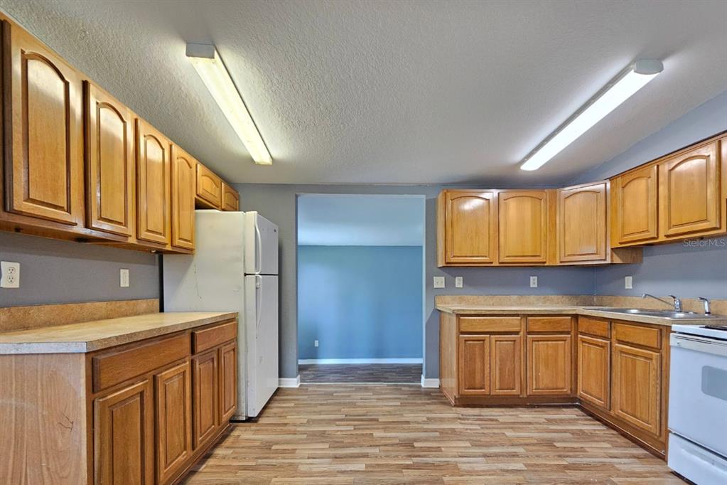A kitchen with wood cabinets, laminate countertops, white appliances, and wood-look flooring — 2431 CANNON STREET, LAKELAND, FL