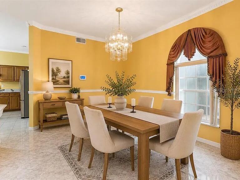 A dining room with yellow walls, a wooden table, upholstered chairs, and a crystal chandelier — 6415 ABBEYDALE COURT, ORLANDO, FL