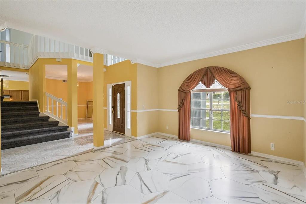 An entryway and living area feature marble-look tile flooring, yellow walls, and a grand staircase — 6415 ABBEYDALE COURT, ORLANDO, FL
