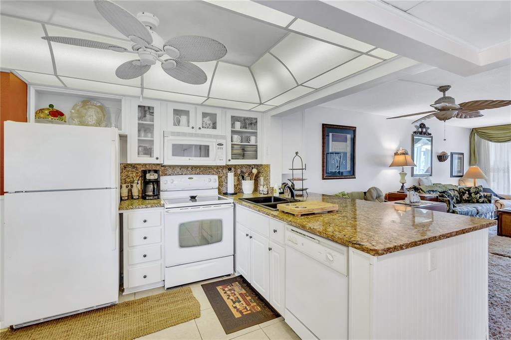 A kitchen with white cabinets, granite countertops, and a ceiling fan, open to a living area — 12300 VONN ROAD UNIT 1102, LARGO, FL