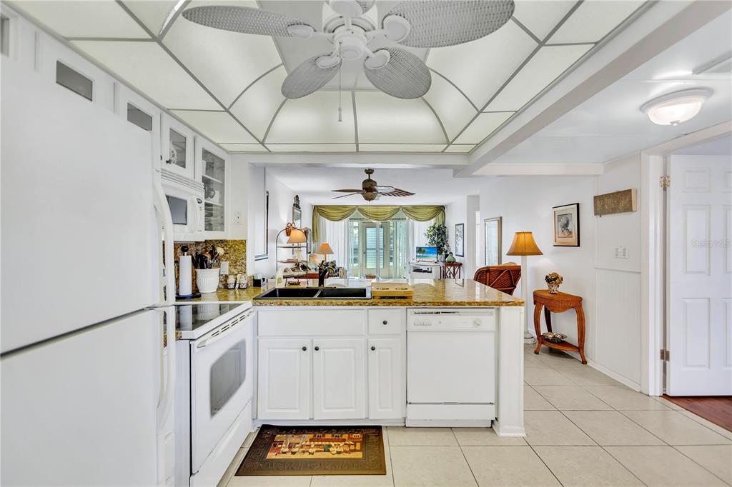 A white kitchen with granite countertops opens into a living area with a ceiling fan — 12300 VONN ROAD UNIT 1102, LARGO, FL