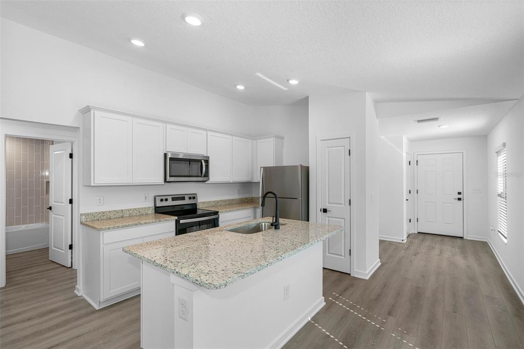A kitchen features white cabinets, granite countertops, a center island, and light wood-look flooring — 15306 SCAUP DUCK ROAD, WEEKI WACHEE, FL