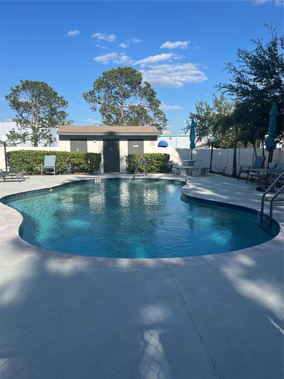 A swimming pool with a concrete deck sits in front of a small utility building — 2651 MICHAEL PLACE UNIT 307, DUNEDIN, FL