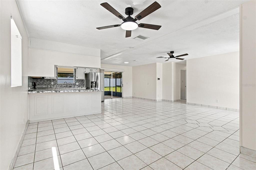 A bright, open-concept kitchen and living area features white cabinetry, tile flooring, and ceiling fans — 1719 JULIAN LN DRIVE, TAMPA, FL