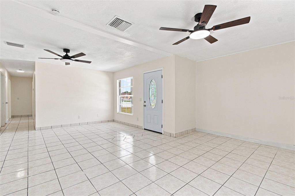 An empty room with light-colored tile flooring, two ceiling fans, and a white front door — 1719 JULIAN LN DRIVE, TAMPA, FL