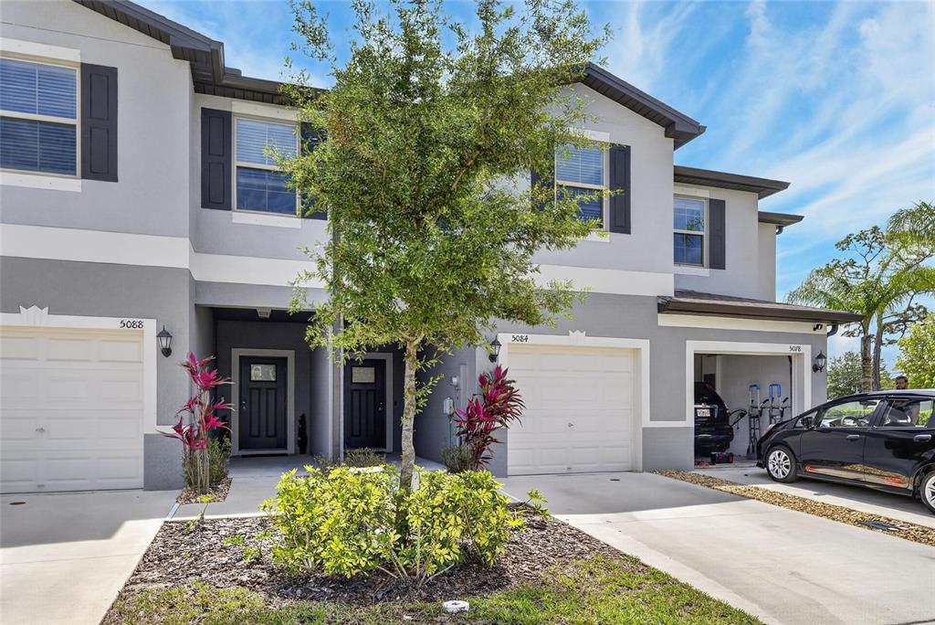 A row of multi-story townhomes with gray stucco facades, garages, and a central tree — 5084 FORUM BLVD, HOLIDAY, FL