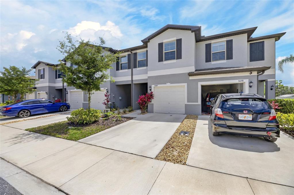A row of two-story townhomes with gray stucco facades, attached garages, and concrete driveways — 5084 FORUM BLVD, HOLIDAY, FL