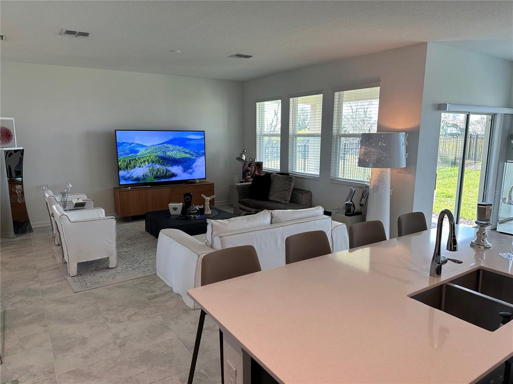 A living room with white furniture and a large television opens to a kitchen island — 8946 FLUFFY LIE COURT, DAVENPORT, FL