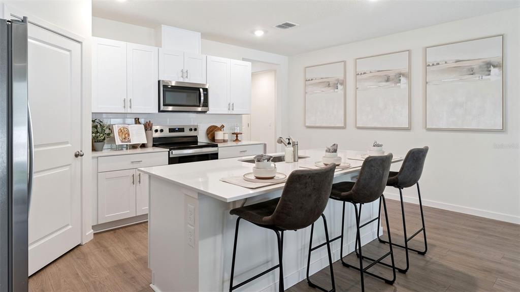 A kitchen features white cabinets, a central island with bar stools, and stainless steel appliances — 103 HERRING LANE, POINCIANA, FL