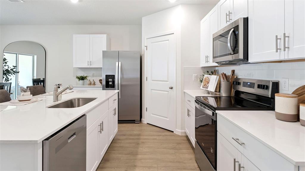 A modern kitchen features white cabinets, stainless steel appliances, and a large quartz-topped island — 103 HERRING LANE, POINCIANA, FL