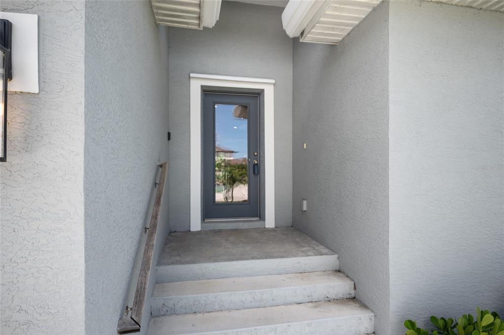 A gray front door with a glass panel is accessed by concrete steps and a railing — 315 SWEETWATER DRIVE, ROTONDA WEST, FL