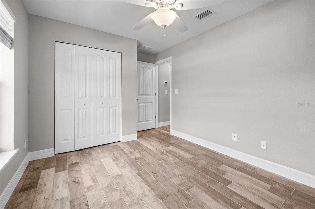 An empty bedroom features light gray walls, wood-look tile flooring, and white bi-fold closet doors — 315 SWEETWATER DRIVE, ROTONDA WEST, FL