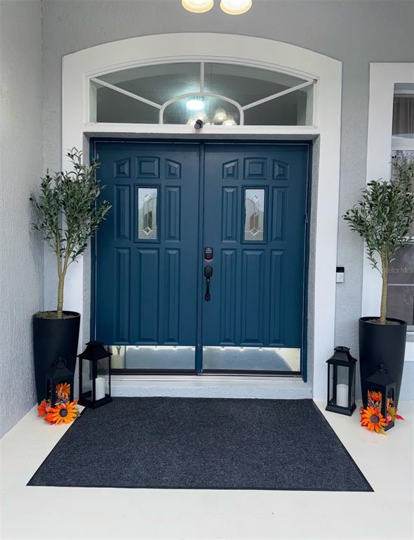 A blue double front door with a transom window is flanked by two potted trees — 426 CARDINAL COURT, KISSIMMEE, FL