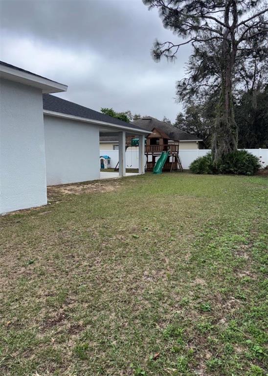 A backyard features a covered patio, a wooden playset with a slide, and a large tree — 426 CARDINAL COURT, KISSIMMEE, FL