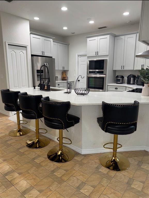 A kitchen features white cabinetry, a large quartz island with four black barstools, and tile flooring — 426 CARDINAL COURT, KISSIMMEE, FL